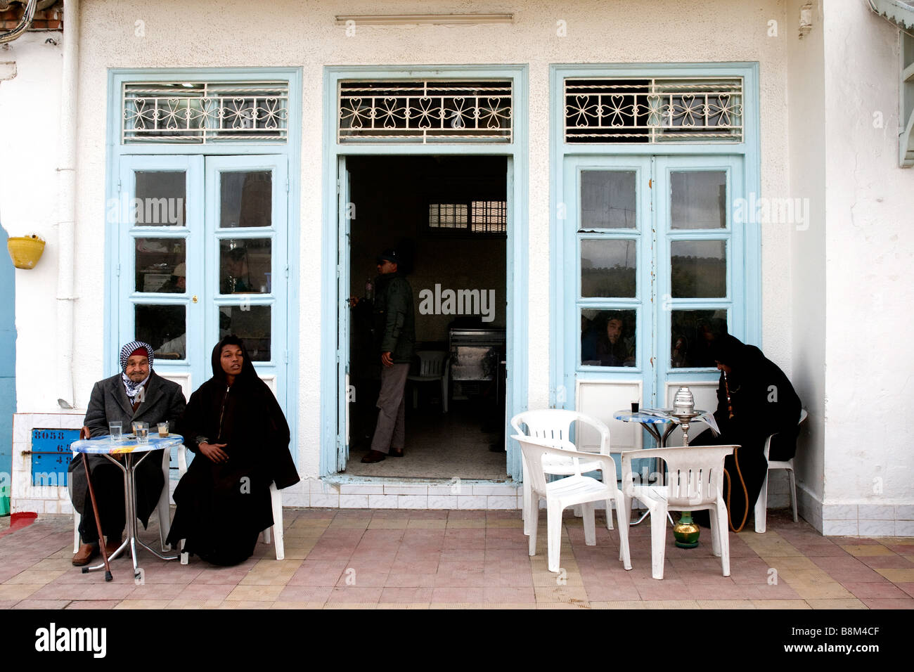 Placcato vivamente contro la mattina chill tre uomini, uno con una rivista e tubo di acqua, rilassarsi al di fuori di un café di Testour, Tunisia Foto Stock