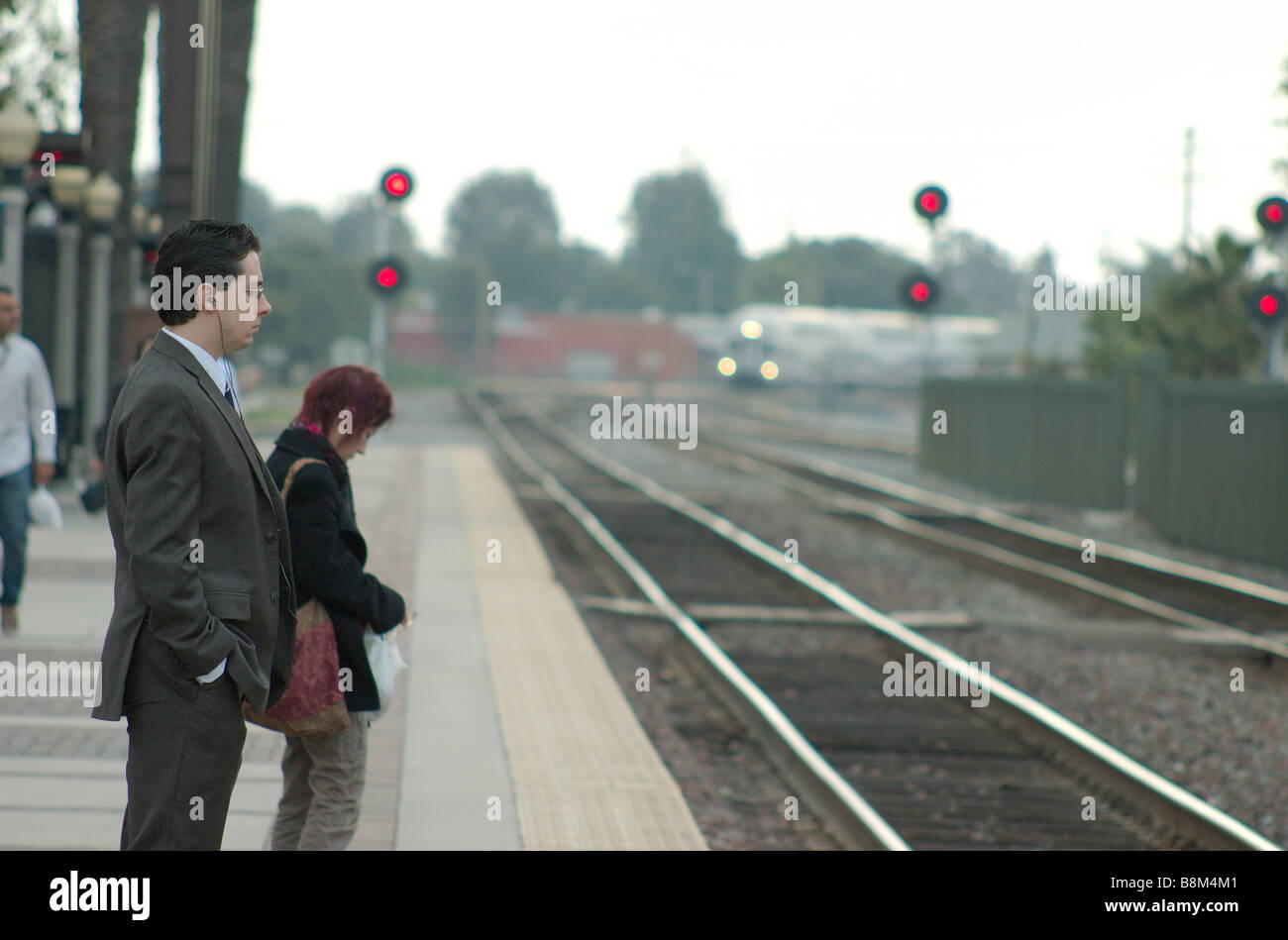 Un uomo d affari con un lettore MP3 in attesa del suo treno per arrivare Foto Stock