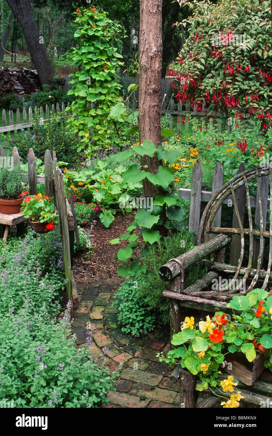 Un vitigno rustico e locusta sedia log nestels besdie un cancello a spiovente in un paese dooryard orto di erbe aromatiche e di verdura. Foto Stock