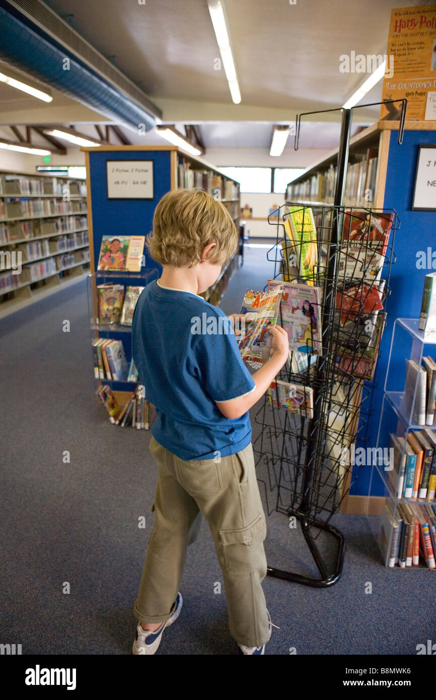 Bambino di otto anni la lettura di un libro a fumetti in una biblioteca pubblica Foto Stock