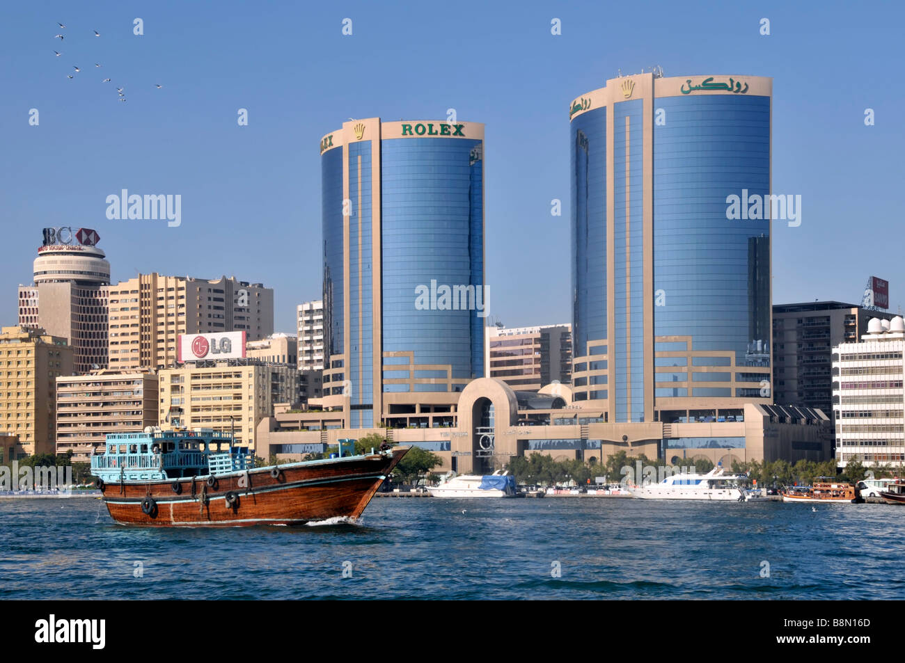 Dubai torri gemelle con la Rolex advert & edificio di moderna architettura urban skyline close up passando dhow barca sul Fiume Dubai EMIRATI ARABI UNITI Medio Oriente Asia Foto Stock