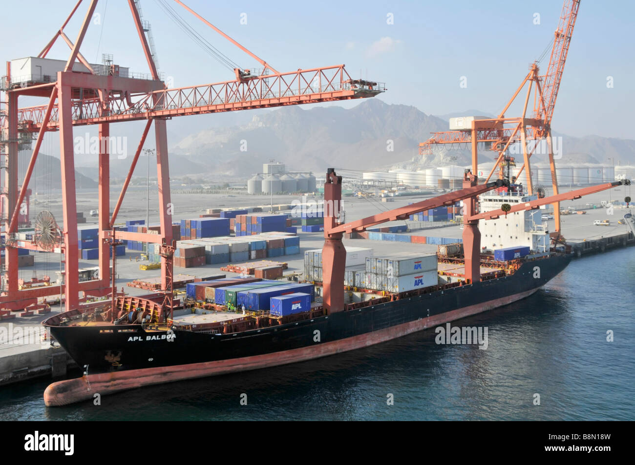 Boxship al porto di Fujairah sul Golfo di Oman contenitori accatastati su banchina e container nave accanto con bulbo prua Foto Stock