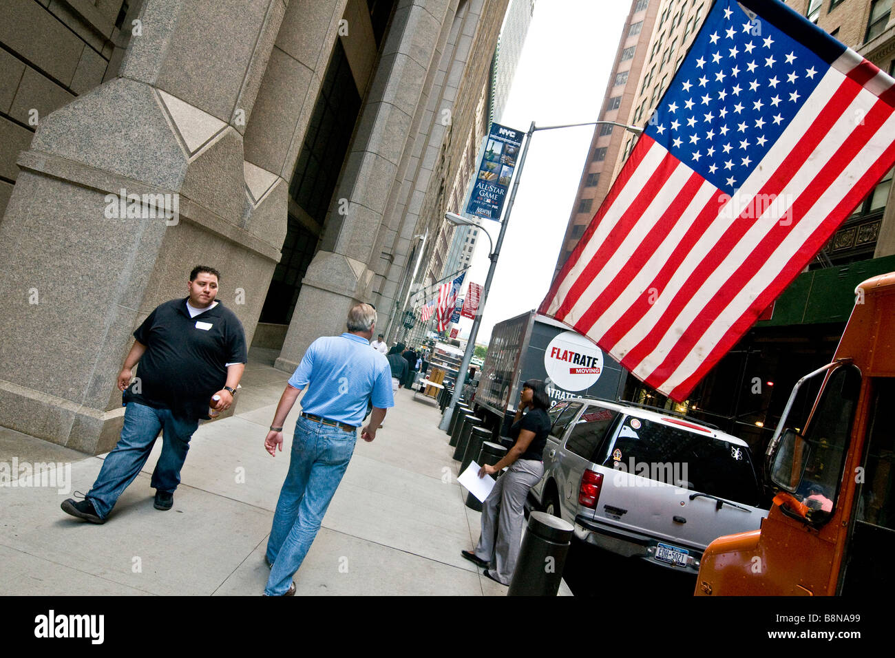 I pedoni a camminare lungo il marciapiede in Manhattan con una grande bandiera americana, Foto Stock