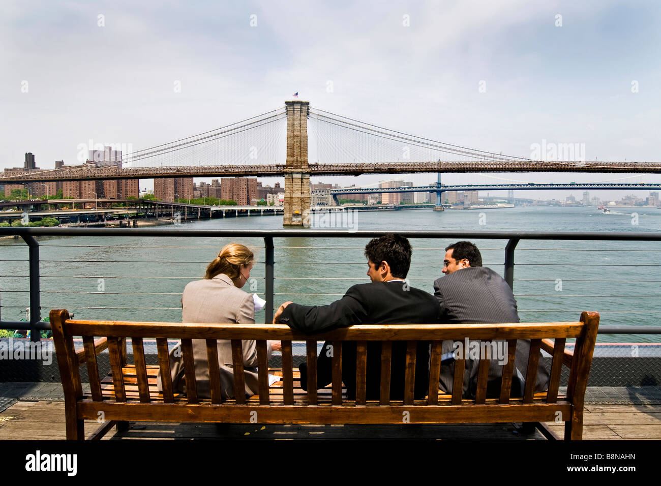 Due uomini e una donna in officewear seduta su una panchina di fronte al Ponte di Brooklyn. Foto Stock
