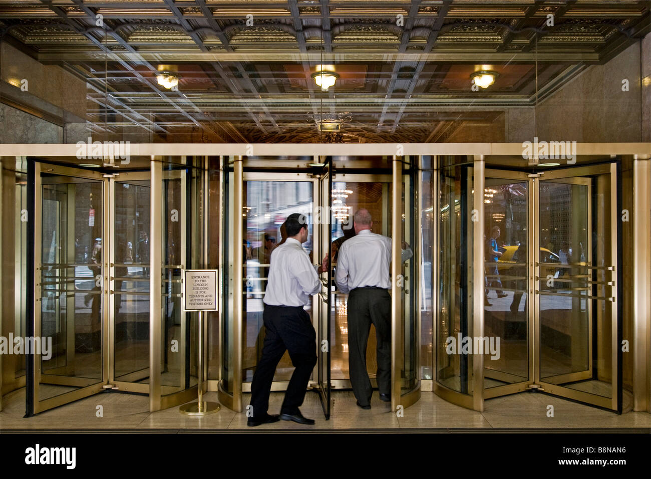 Imprenditori di entrare nel grandioso foyer di un edificio attraverso una delle numerose porte girevoli di vetro Foto Stock