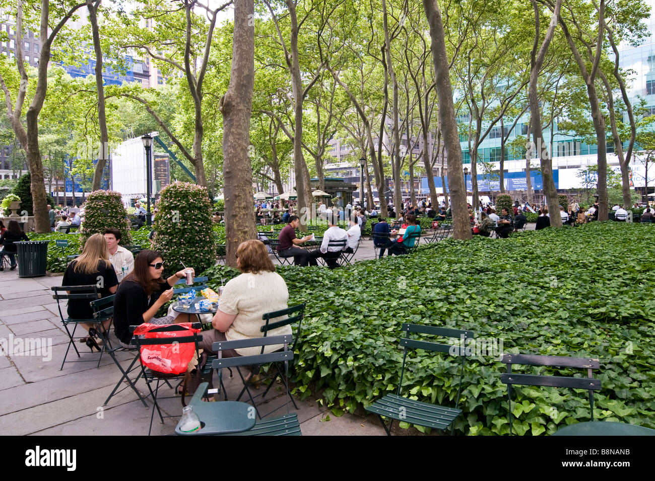 Persone seduti ai tavolini sotto gli alberi alti in un giardino pubblico Foto Stock