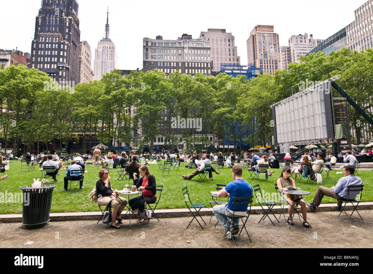 Le persone sedute a tavoli piccoli alberi in un giardino pubblico Foto Stock