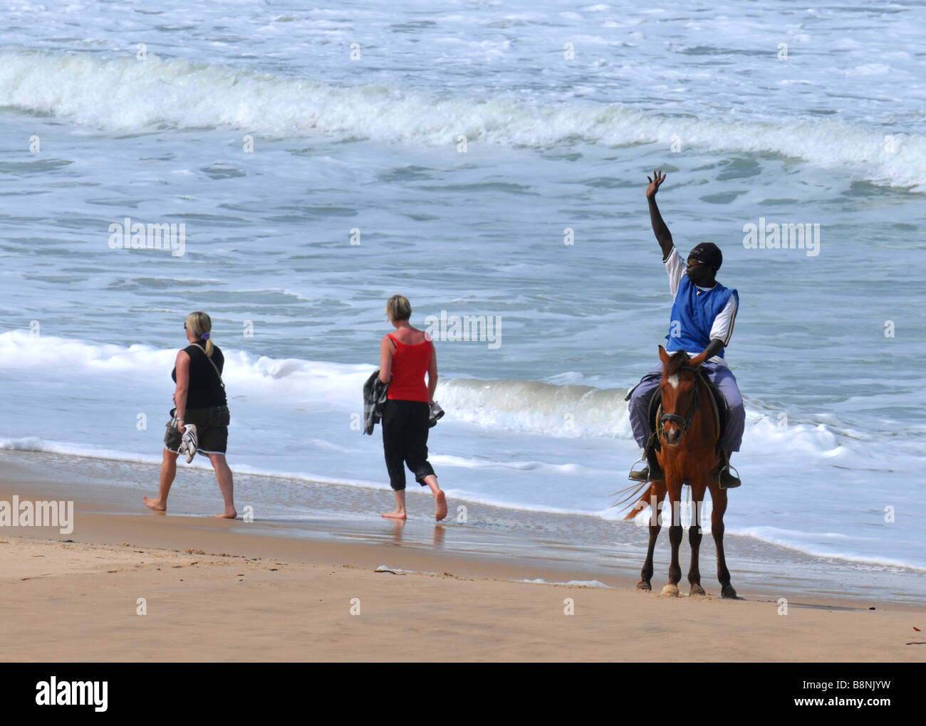 Uomo locale a cavallo onde ai turisti femmina sulla spiaggia, Gambia, "West Africa" Foto Stock