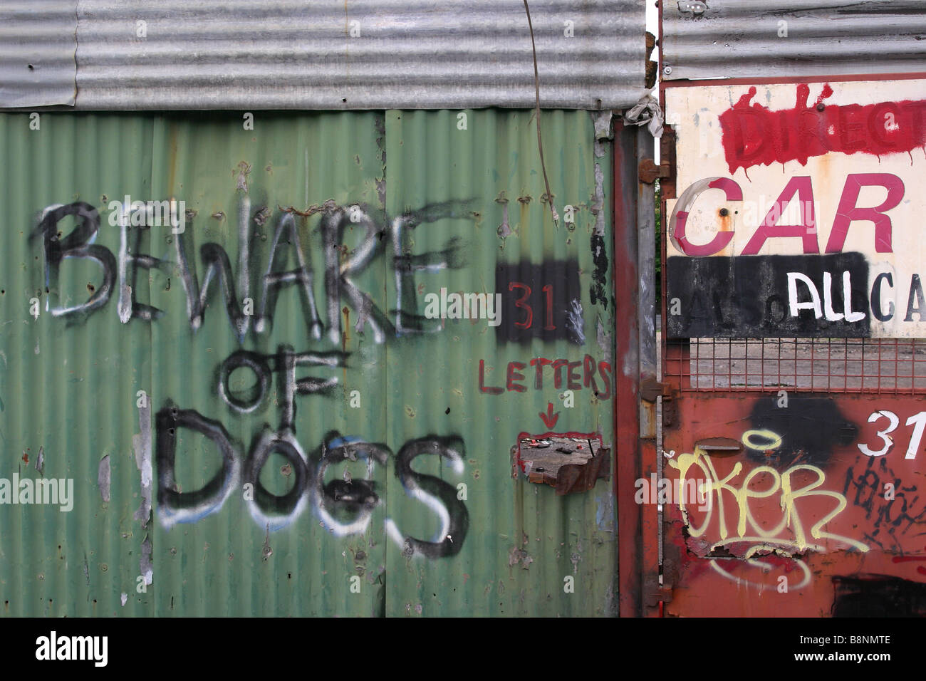 Attenzione ai cani dipinta su ondulato recinzione in ferro del commerciante di rottame in una zona industriale. Foto Stock