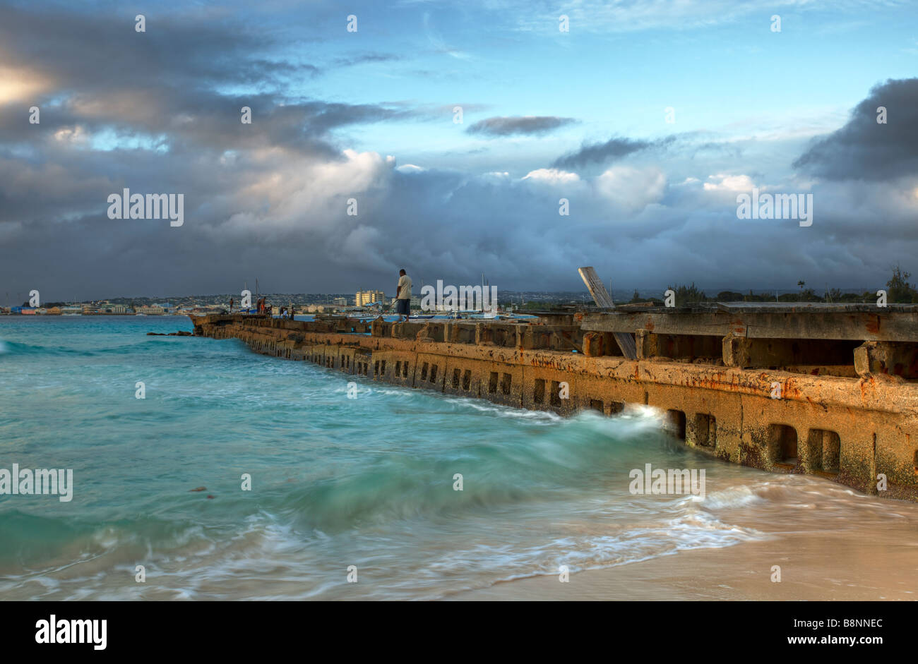 Un uomo pesca in un vecchio pontile in legno in "Spiaggia ghiaiosa', San Michele, Barbados Foto Stock