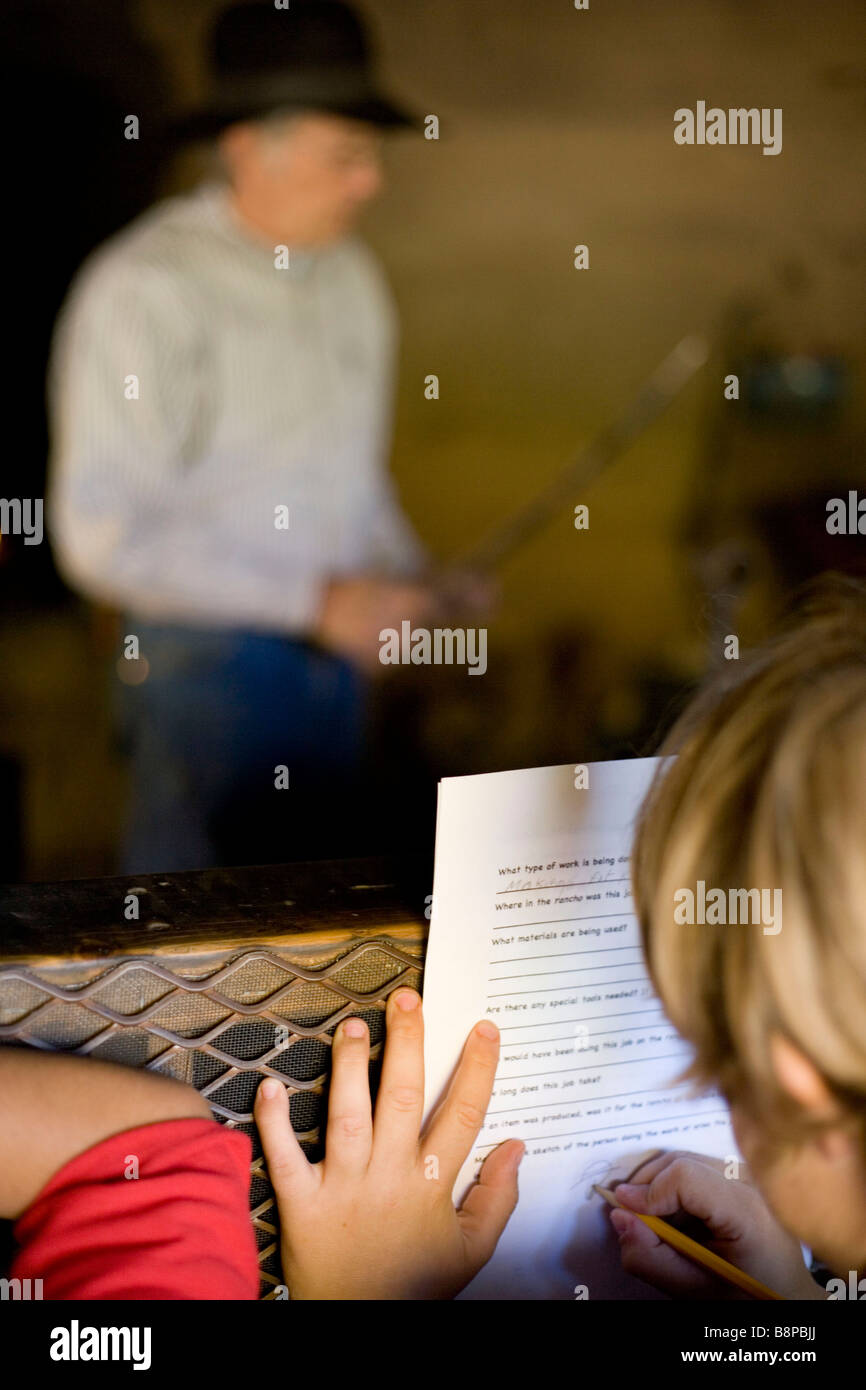 Bambino prendendo appunti su un fieldtrip mentre un fabbro dimostra come egli smelleds, riscalda il metallo per gli strumenti del modulo Foto Stock