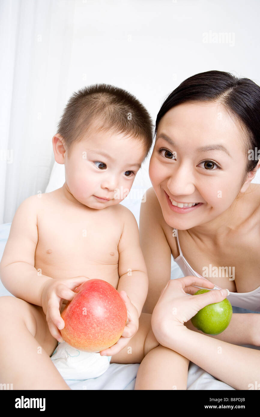 Baby boy e madre sul letto con apple ritratto sorridente Foto Stock