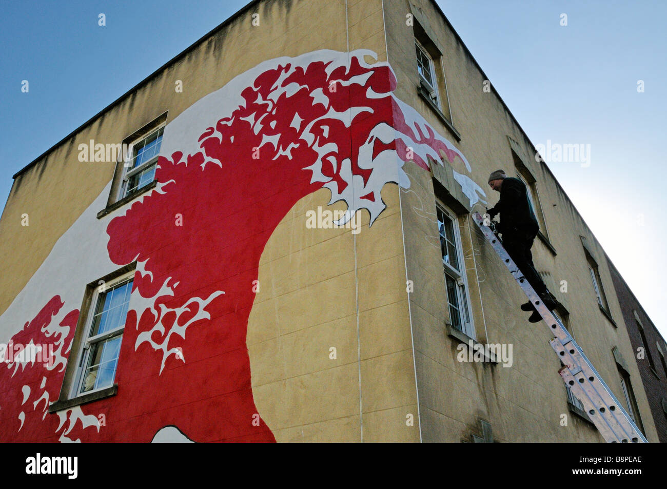 Artista di graffiti sulla parte superiore della scala di pittura murale a parete di onda 'Stokes Croft' area di Bristol Foto Stock