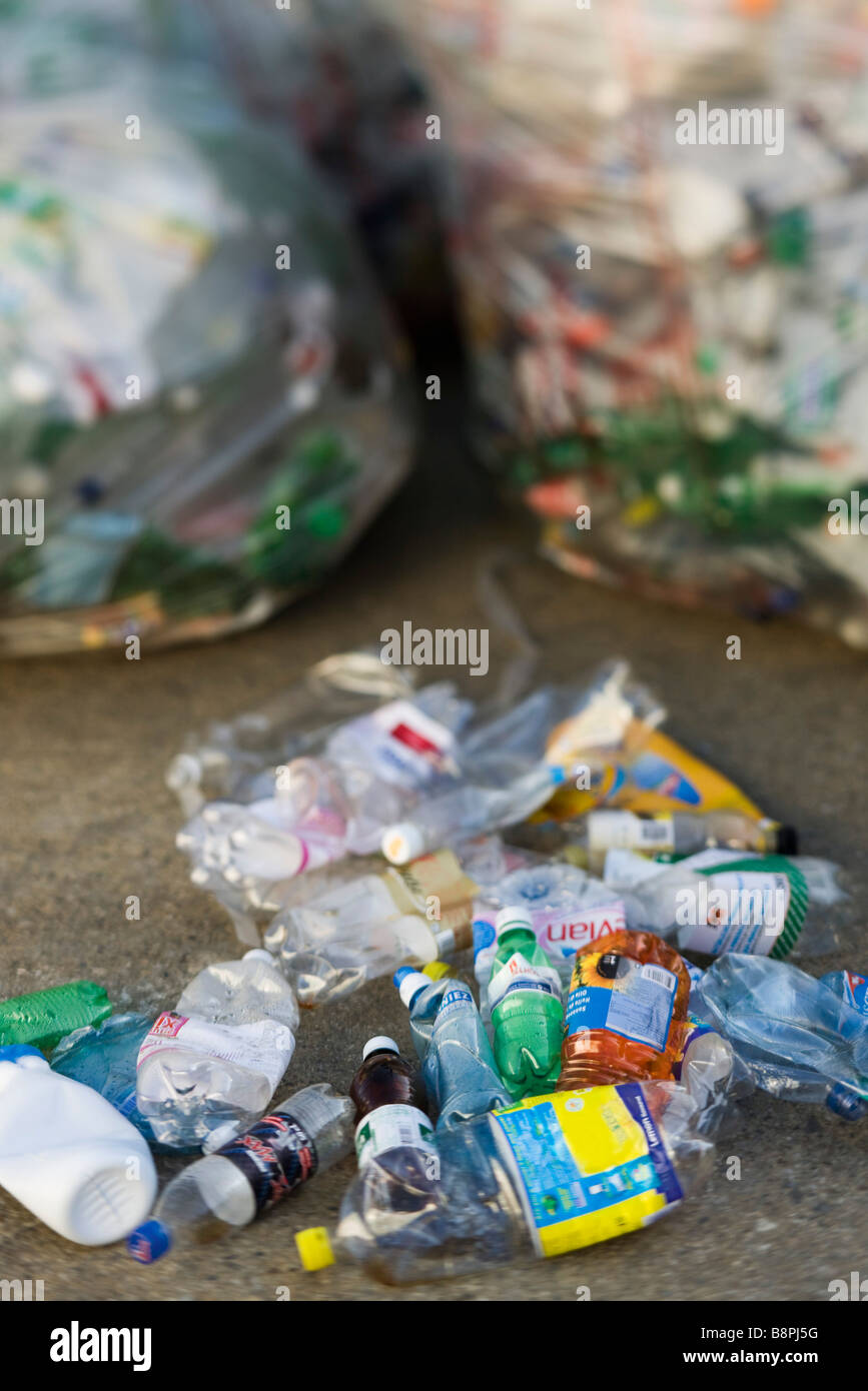 Schiacciate le bottiglie di plastica sul terreno, sacchi della spazzatura in background Foto Stock