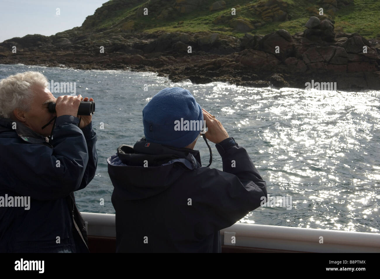 Un giovane con un binocolo visualizza le guarnizioni e la fauna sulle isole orientali a bordo di una barca. Isole Scilly. La Cornovaglia. SW Inghilterra Foto Stock
