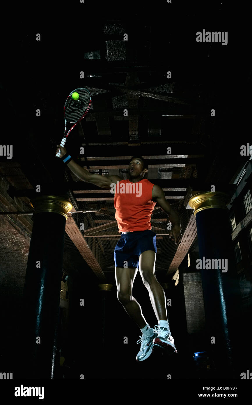 Pratica di tennis di notte, in città / ambiente urbano, giocatore con racchetta pratica sotto archi ferroviari, giocatore maschio Foto Stock