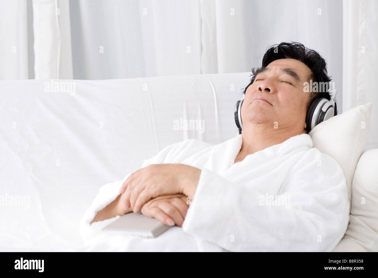Senior Uomo sdraiato sul divano ascoltando musica Foto Stock