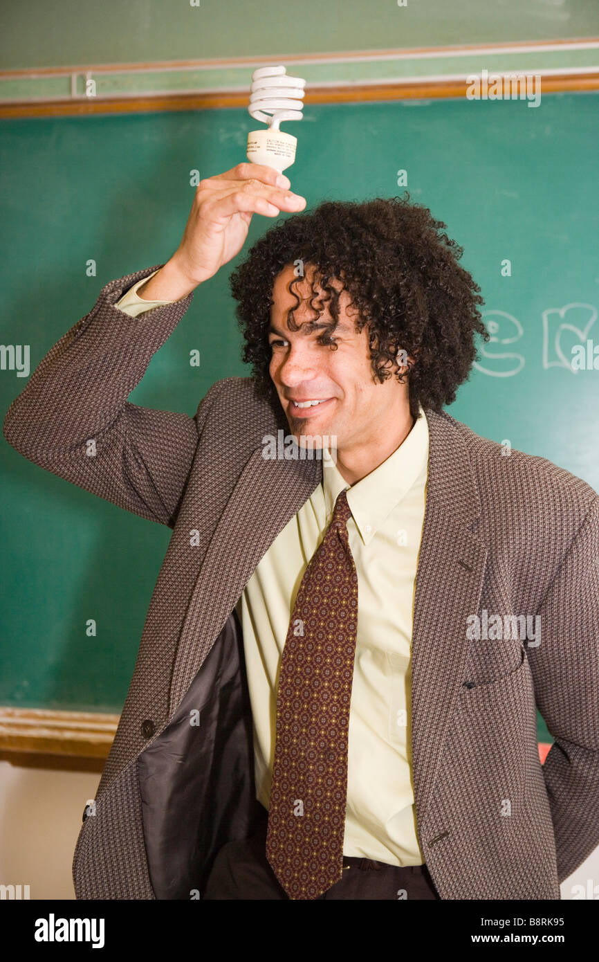 African American insegnante nella scuola pubblica tenendo un efficiente di energia fluorescente compatta lampadina della luce sulla sua testa Foto Stock