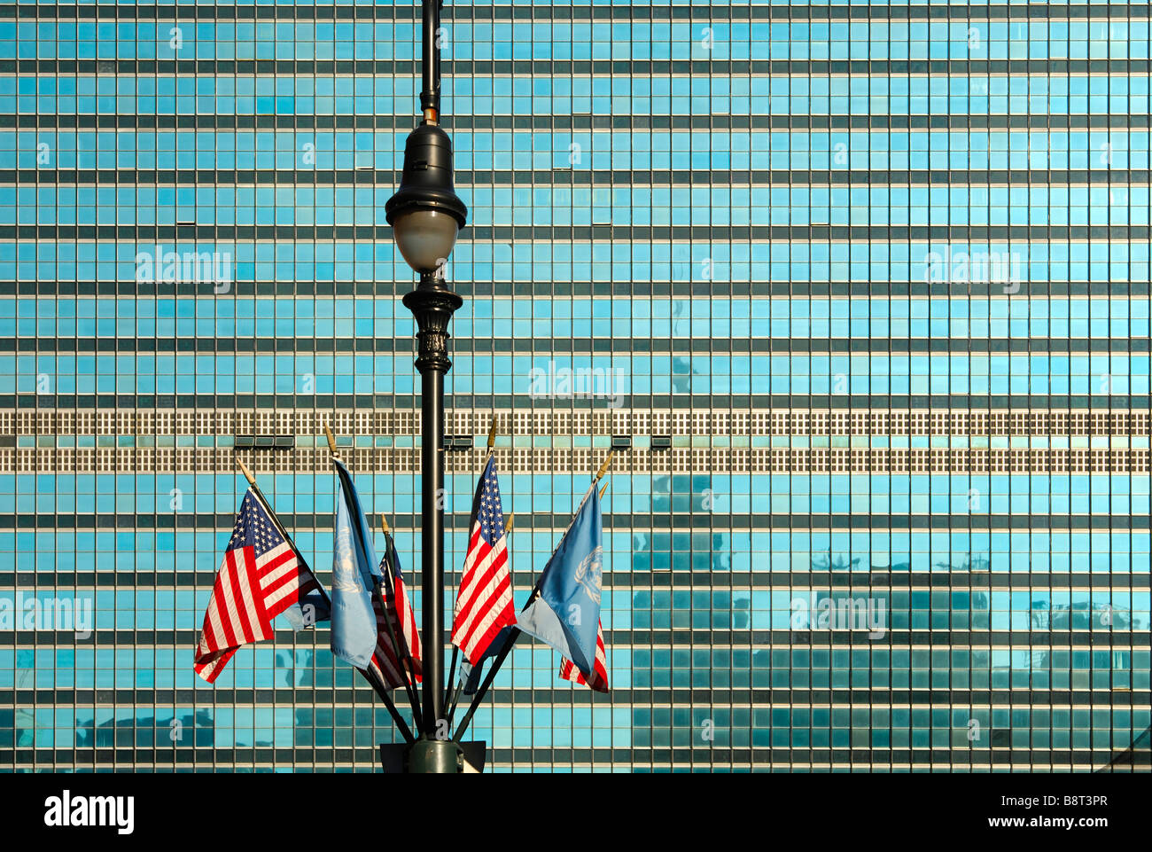 Lampione con ONU e noi le bandiere di fronte alla facciata di vetro del quartier generale delle Nazioni Unite, l'ONU, New York, Stati Uniti d'America Foto Stock