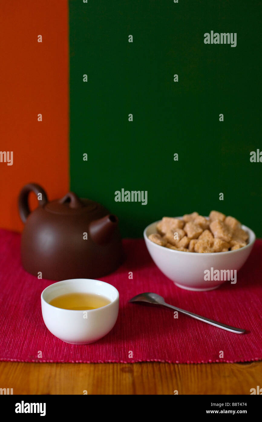 Una tazza di tè, una teiera e una tazza di zucchero di canna cubi. Foto Stock