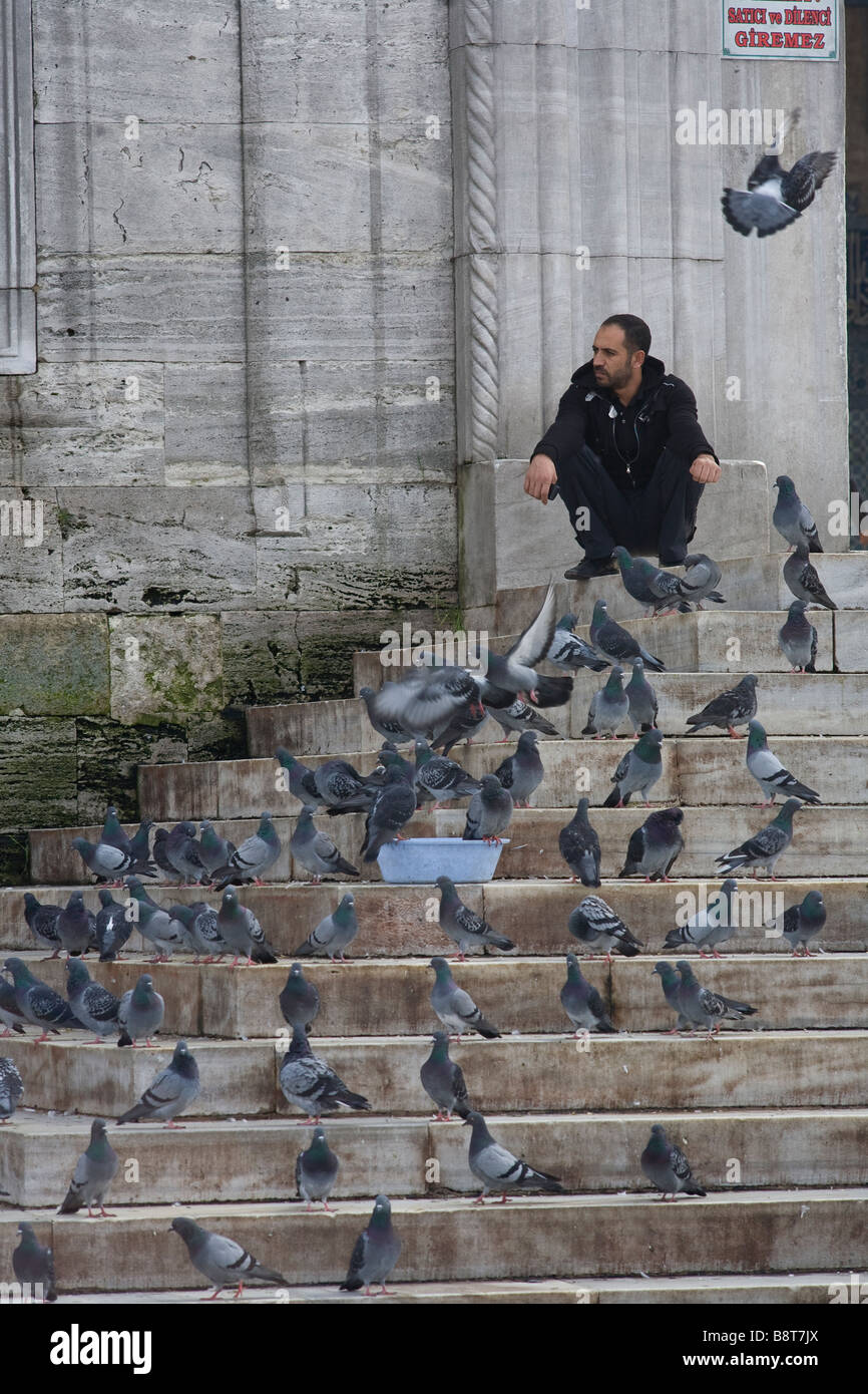 L'uomo circondato da piccioni in attesa all'ingresso della nuova moschea di Istanbul. Foto Stock