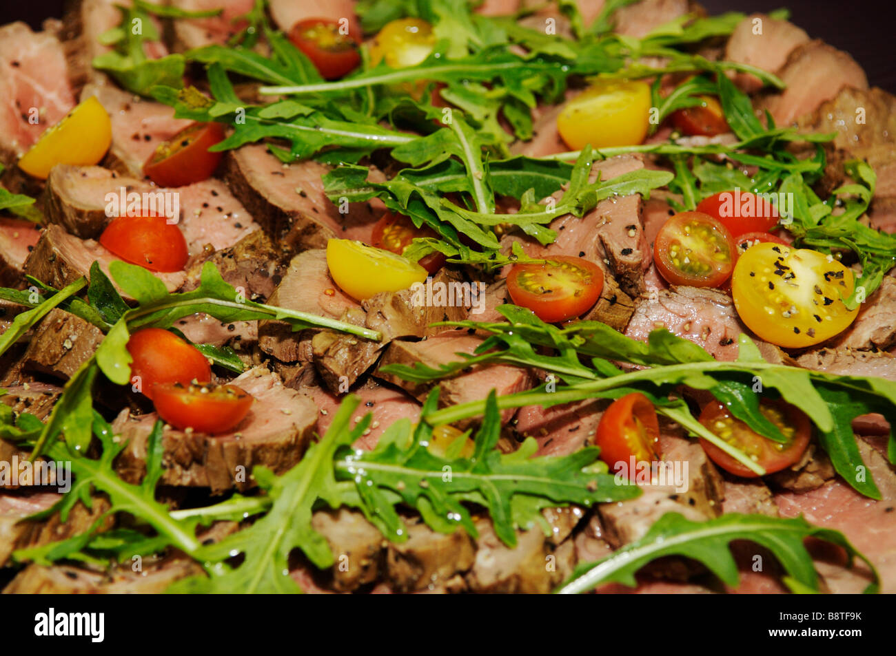 Arrosto di manzo, il giallo e il rosso dei pomodori, insalata di rucola. Foto Stock