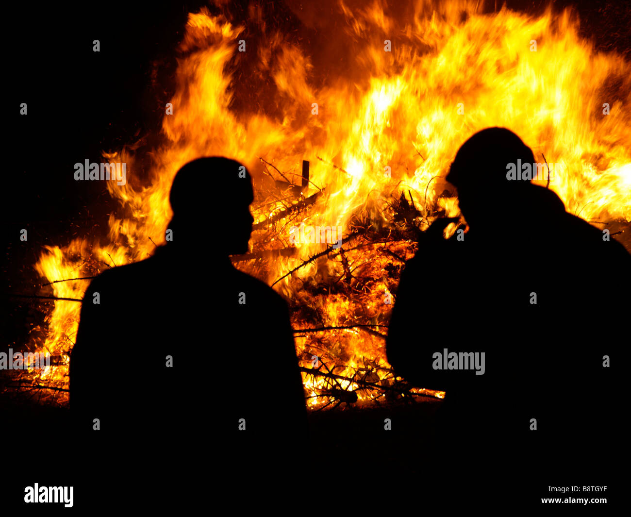 Due uomini profilarsi davanti a un enorme falò di fuoco dalla combustione di vecchi alberi di natale Foto Stock