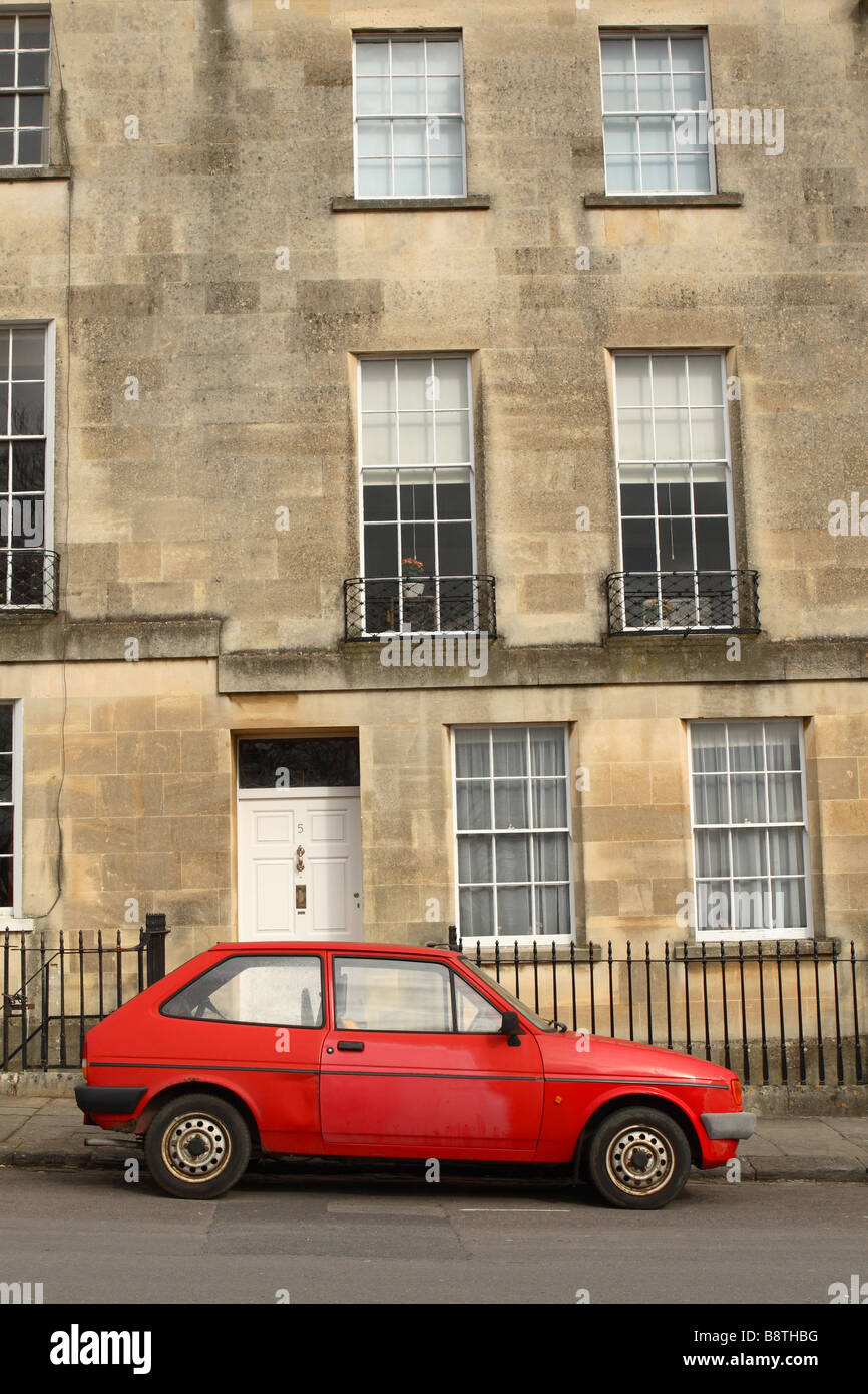 Un vecchio rosso trasandato a buon mercato auto parcheggiate al di fuori di un lusso costoso terrazza georgiana casa in Inghilterra Bath Foto Stock