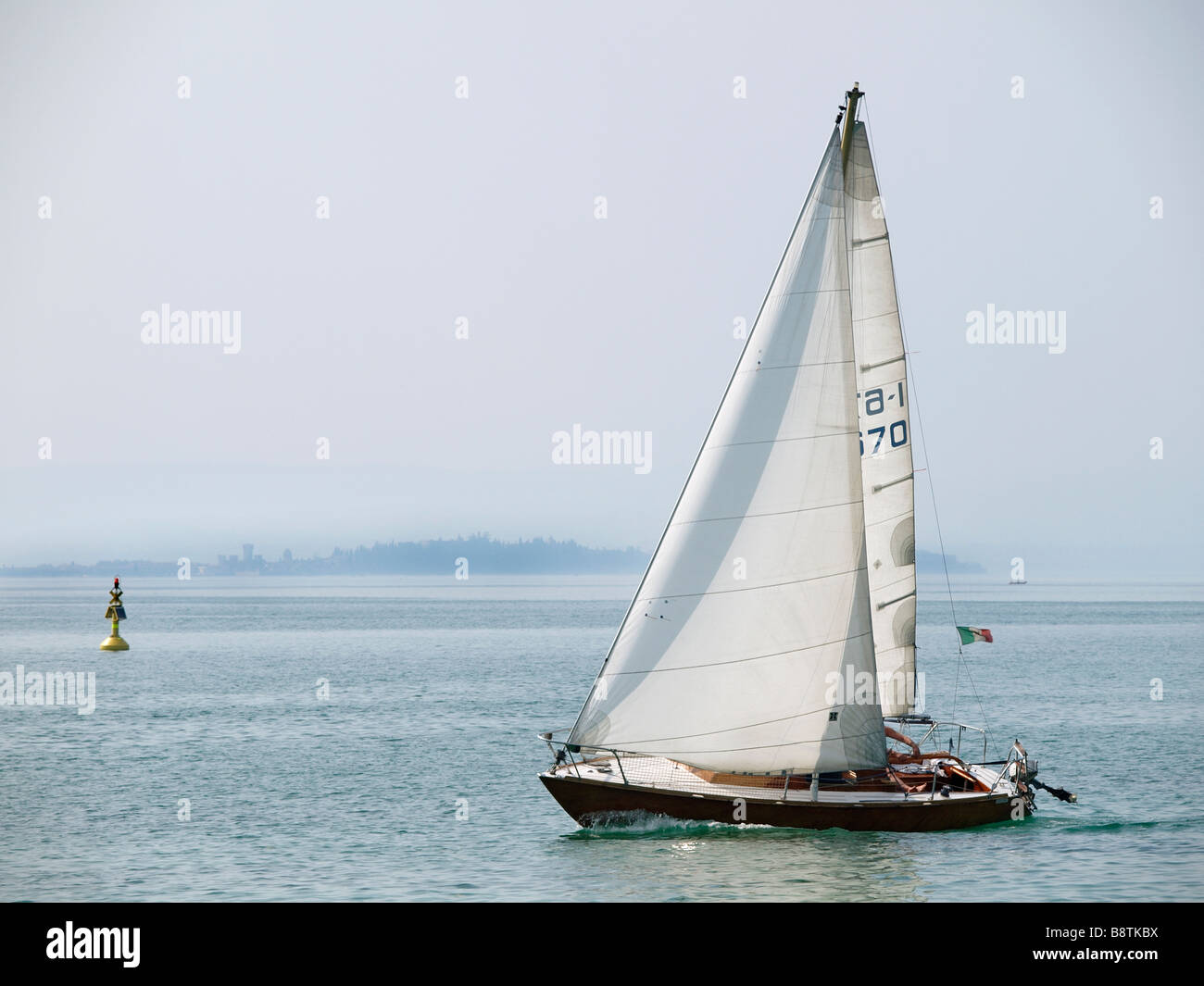 Bellissima in legno classico yacht a vela nei pressi di Peschiera del Garda con lo skyline di Sirmione visibile all'orizzonte. Foto Stock