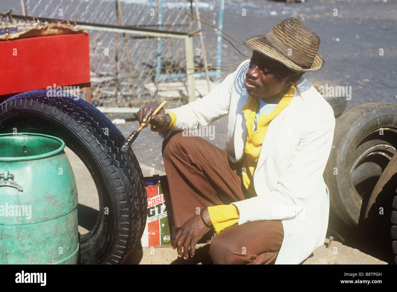 Un uomo in Harare verniciatura pneumatici auto nero, per la rivendita sul mercato, Zimbabwe 1984 Foto Stock