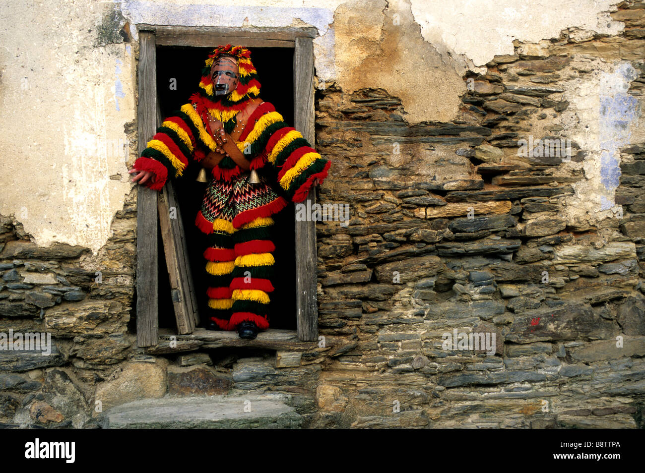 Un uomo vestito con una tradizione 'Caretos' costume incorniciato in una casa colonica porta durante il carnevale di celebrazioni in Podence, Portogallo Foto Stock