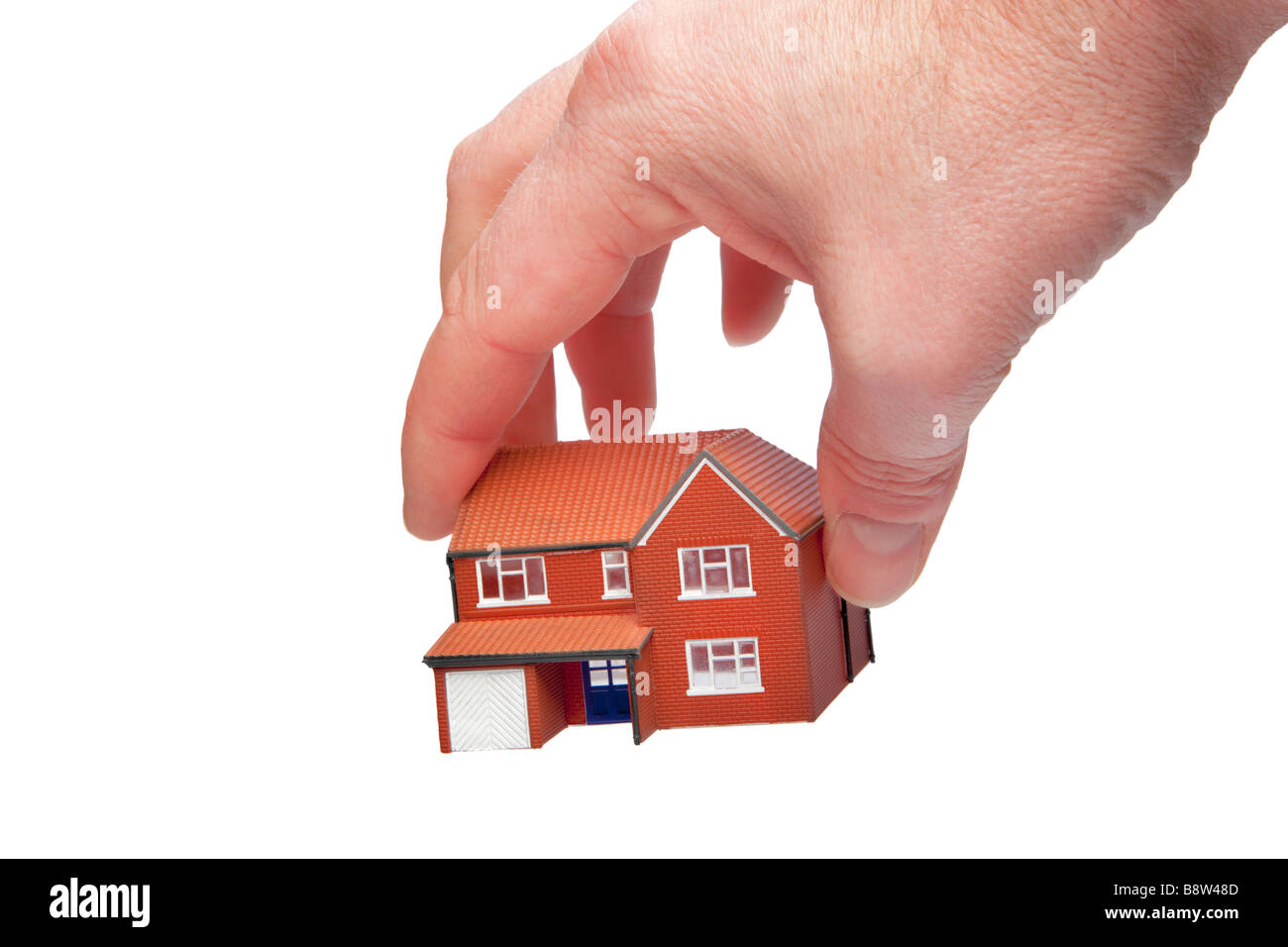 La mano di prelevare una piccola casa isolata su uno sfondo bianco Foto Stock