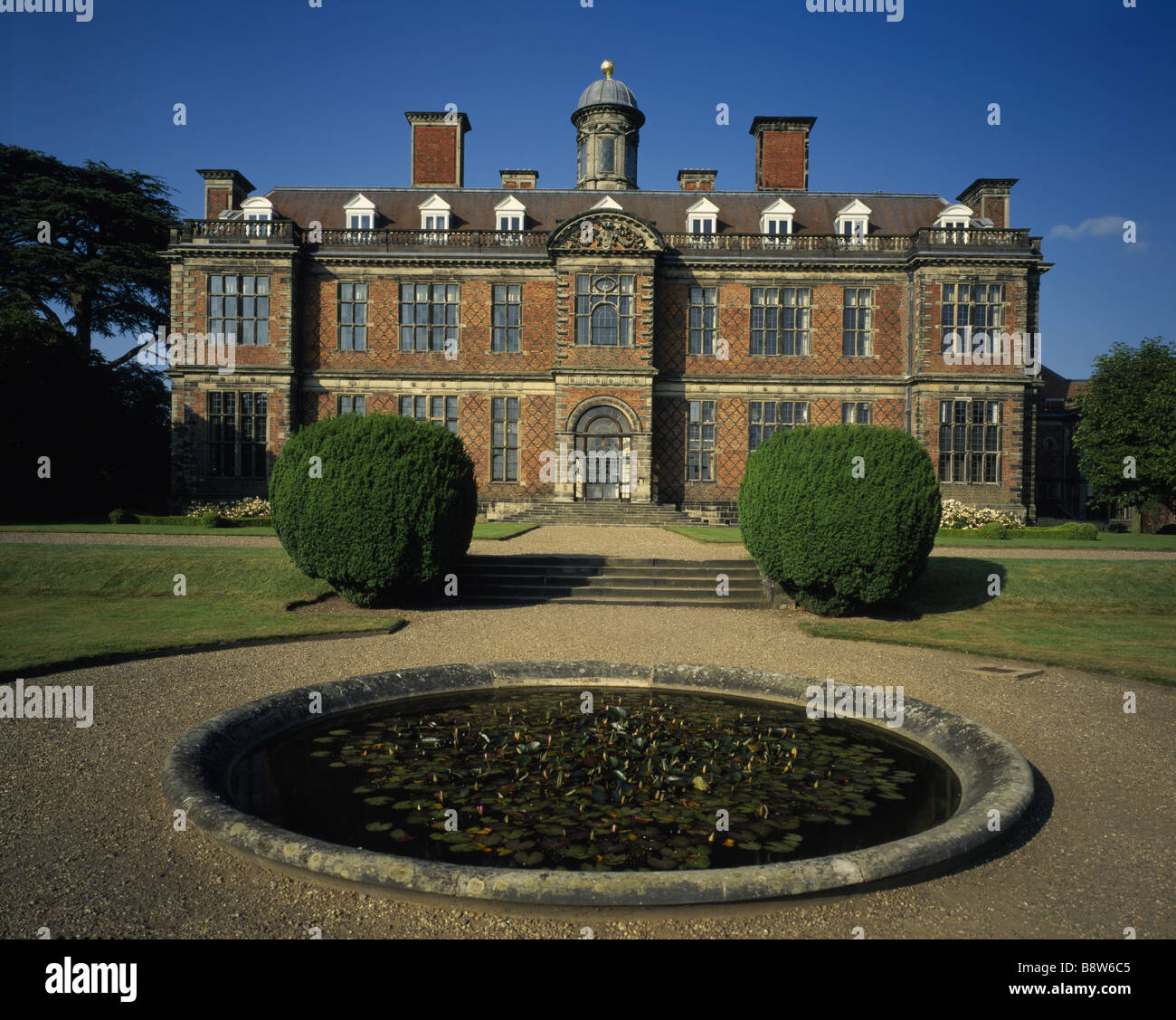Fronte sud di Sudbury Hall spicca contro il cielo blu con il laghetto di gigli in primo piano Foto Stock