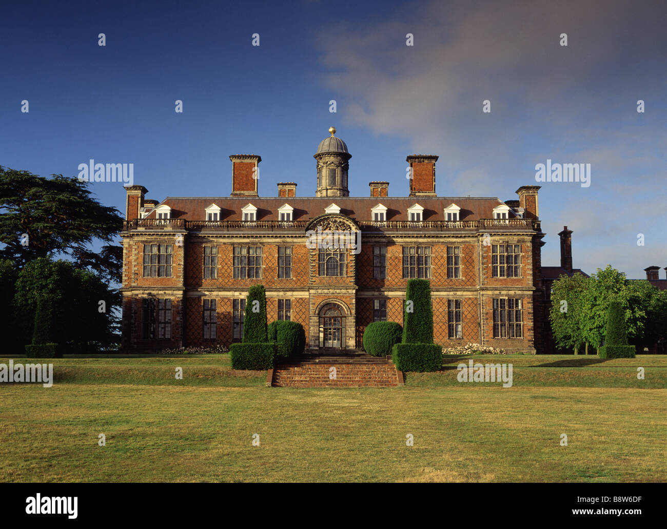 Una vista del fronte sud di Sudbury Hall contro il cielo blu presi da prato con le fasi di mattoni in primo piano Foto Stock
