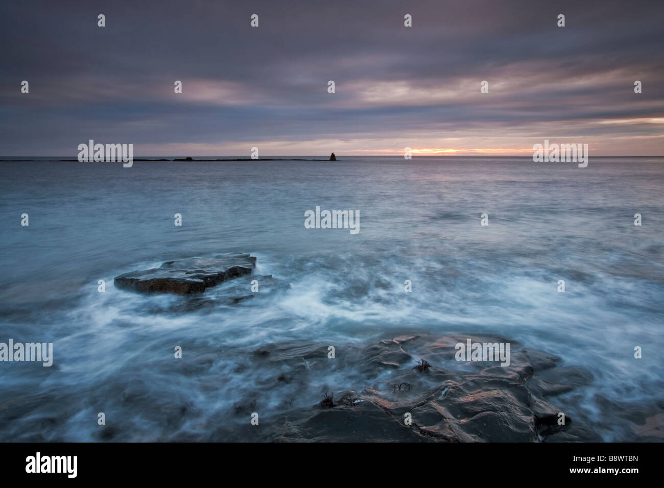 Nero pedana Whin rocce sulla costa Northumbrian immersi nella luce rosa di sunrise Foto Stock
