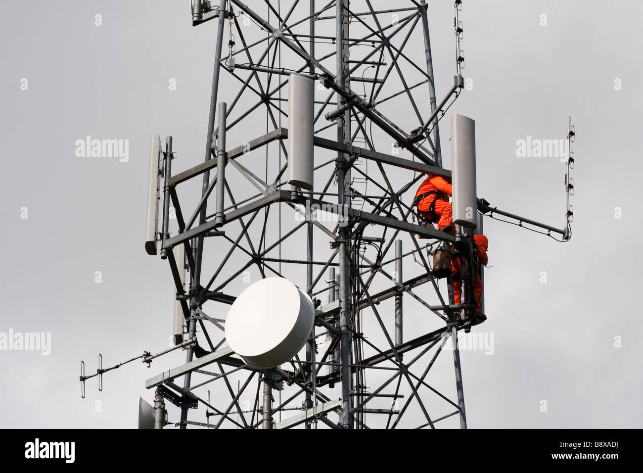 2 gli uomini indossano tute arancioni lavorare in alto su una torre radio Installazione e riparazione di antenne Foto Stock