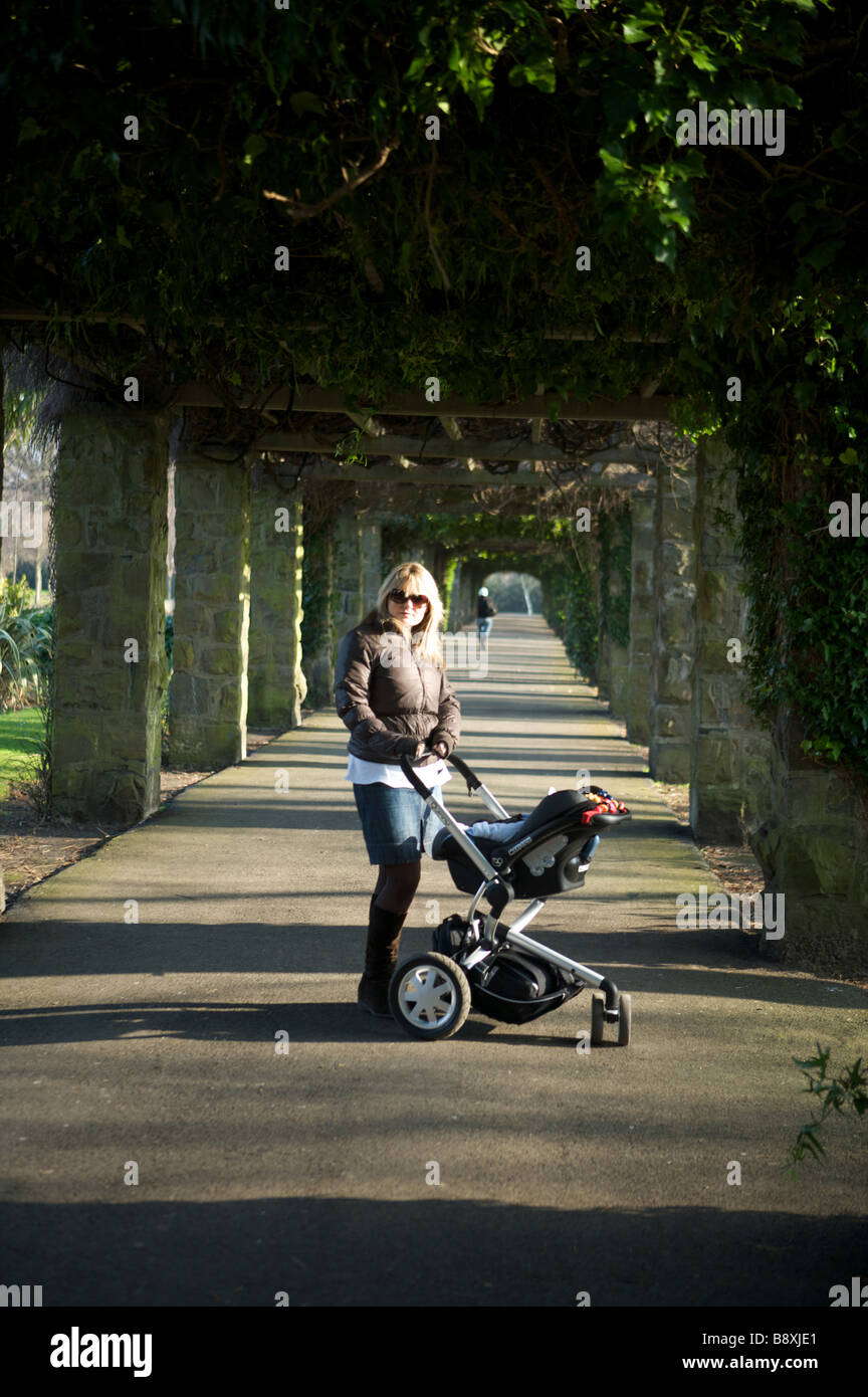 Una giovane madre spinge il suo bambino in un parco in un buggy nero Foto Stock