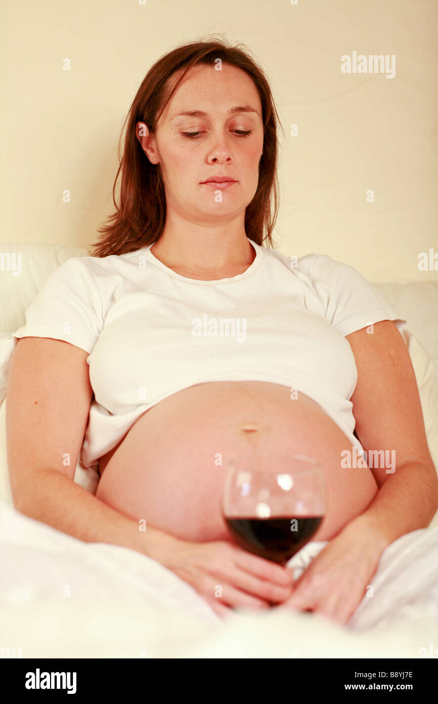Premuto triste fortemente incinta Donna staring al grande bicchiere di vino rosso gradazione mamma infelice gravidanza nocivo per il feto Foto Stock