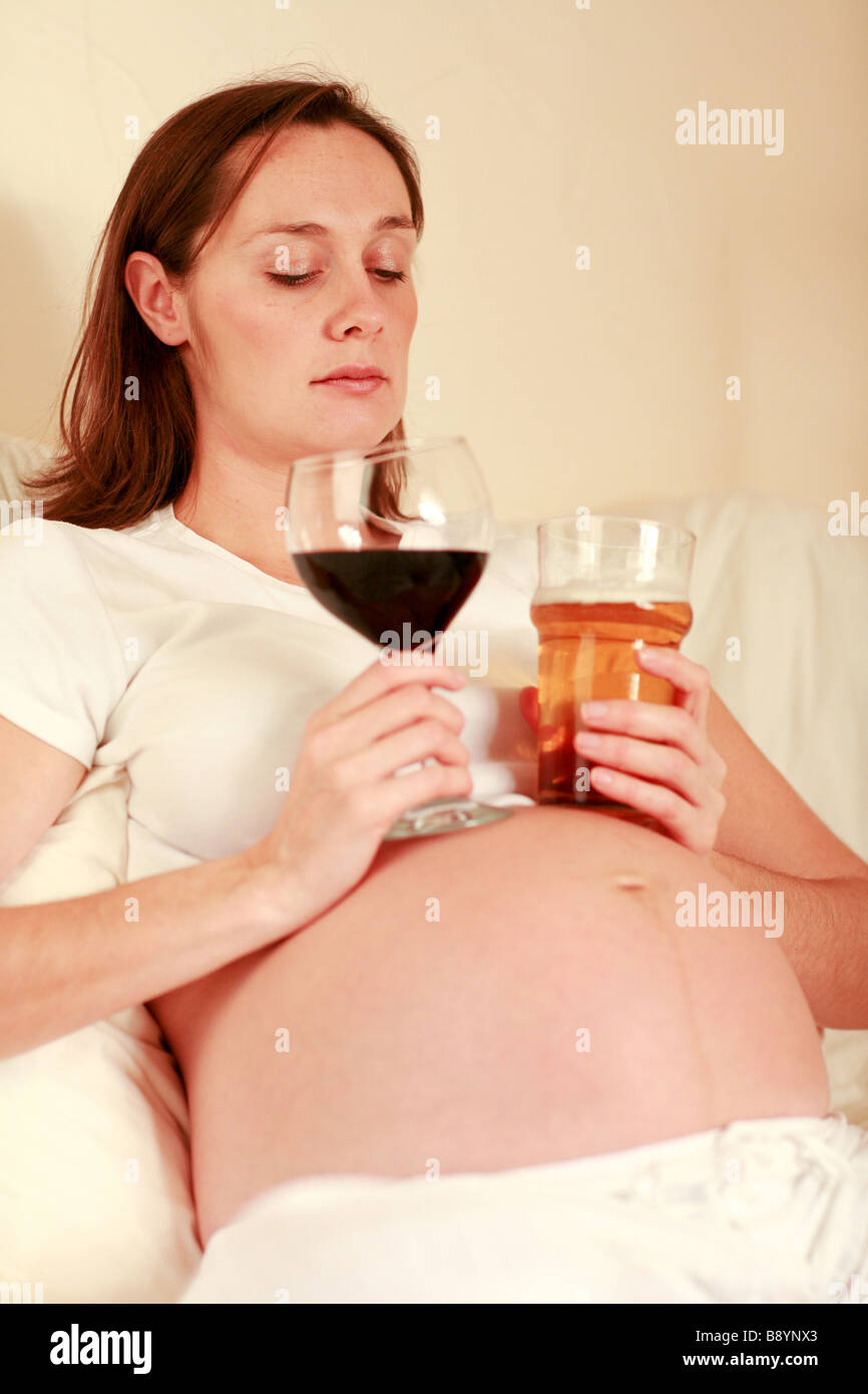Premuto triste fortemente incinta Donna staring al grande bicchiere di vino rosso e una pinta di birra lager gradazione mamma FAS dannosi per il bambino Foto Stock
