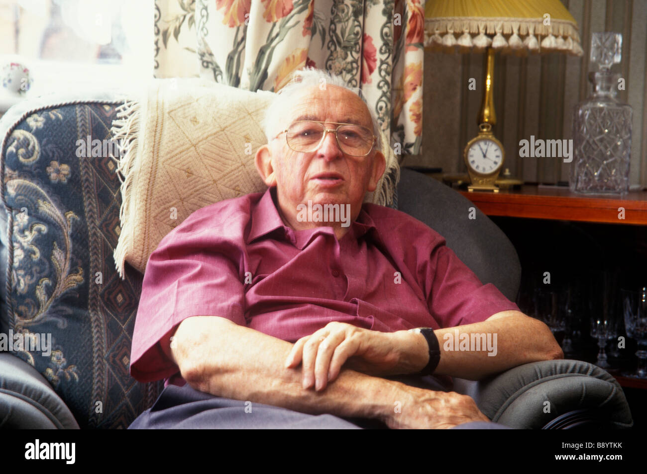 Uomo anziano cercando solitari e isolati in casa con orologio in background Foto Stock