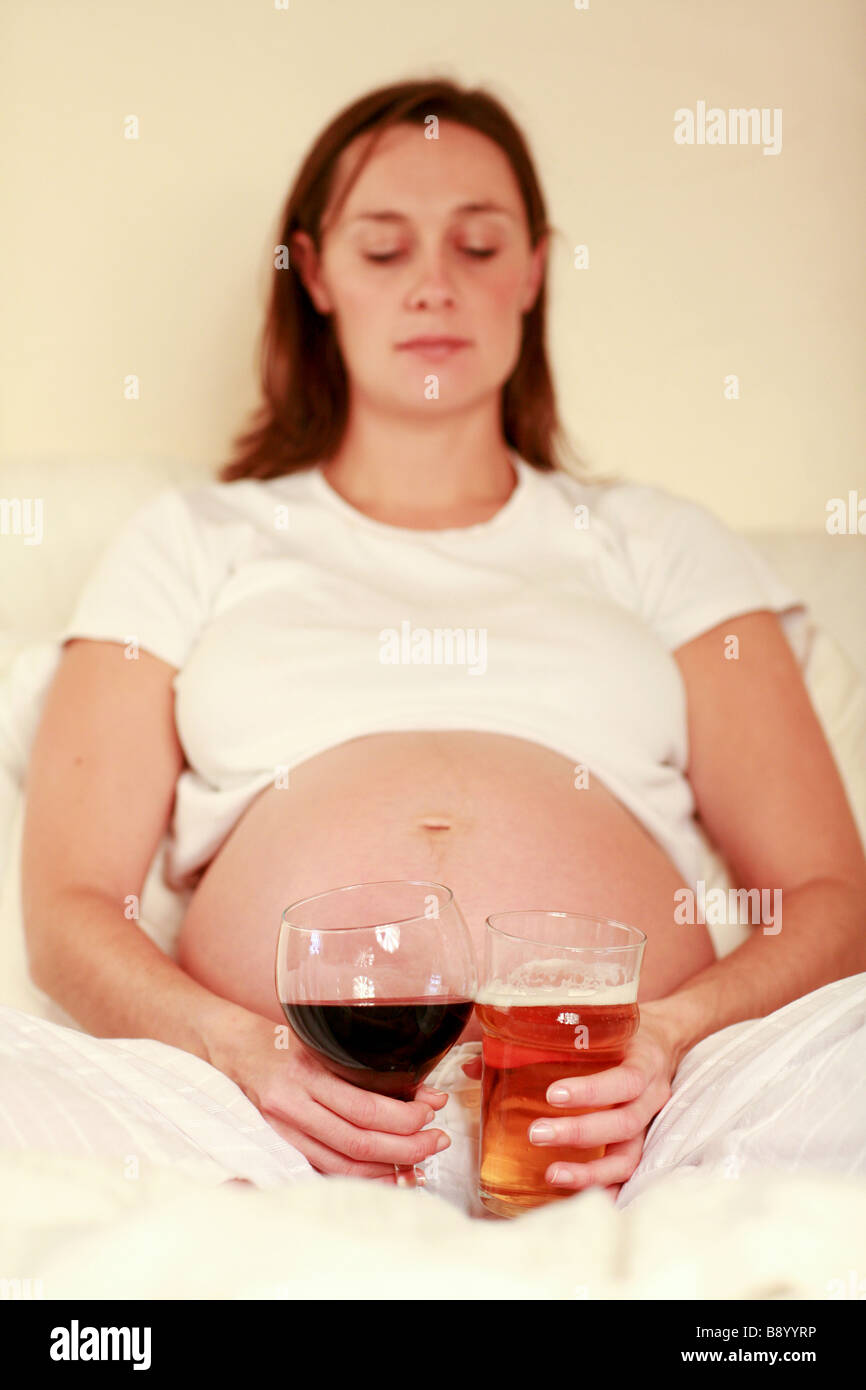 Premuto triste fortemente incinta Donna staring al grande bicchiere di vino rosso e una pinta di birra lager gradazione mamma FAS dannosi per il bambino Foto Stock