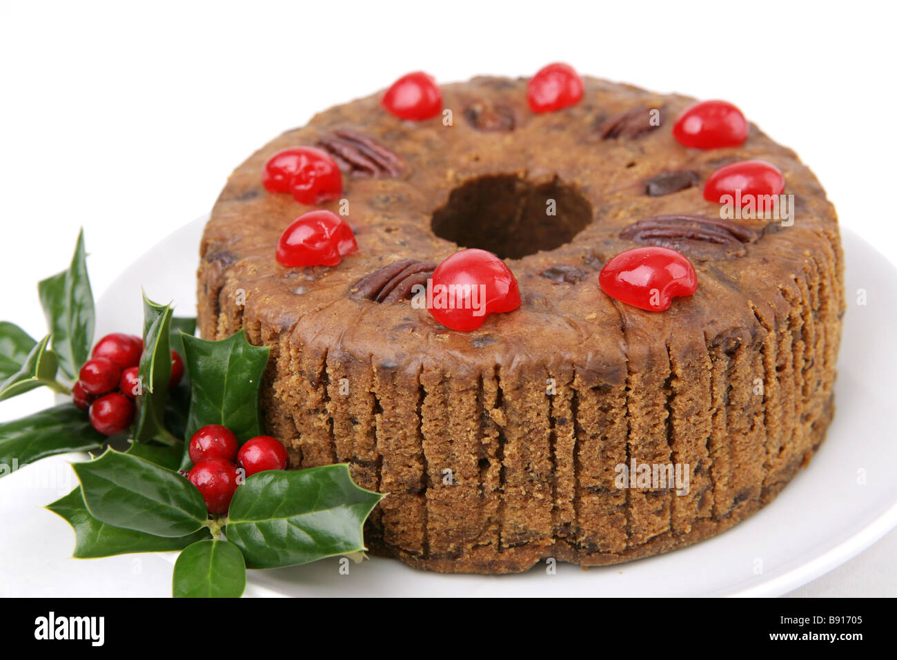 Una bella torta di frutta di Natale guarnita con ciliegie e holly bacche sfondo bianco Foto Stock