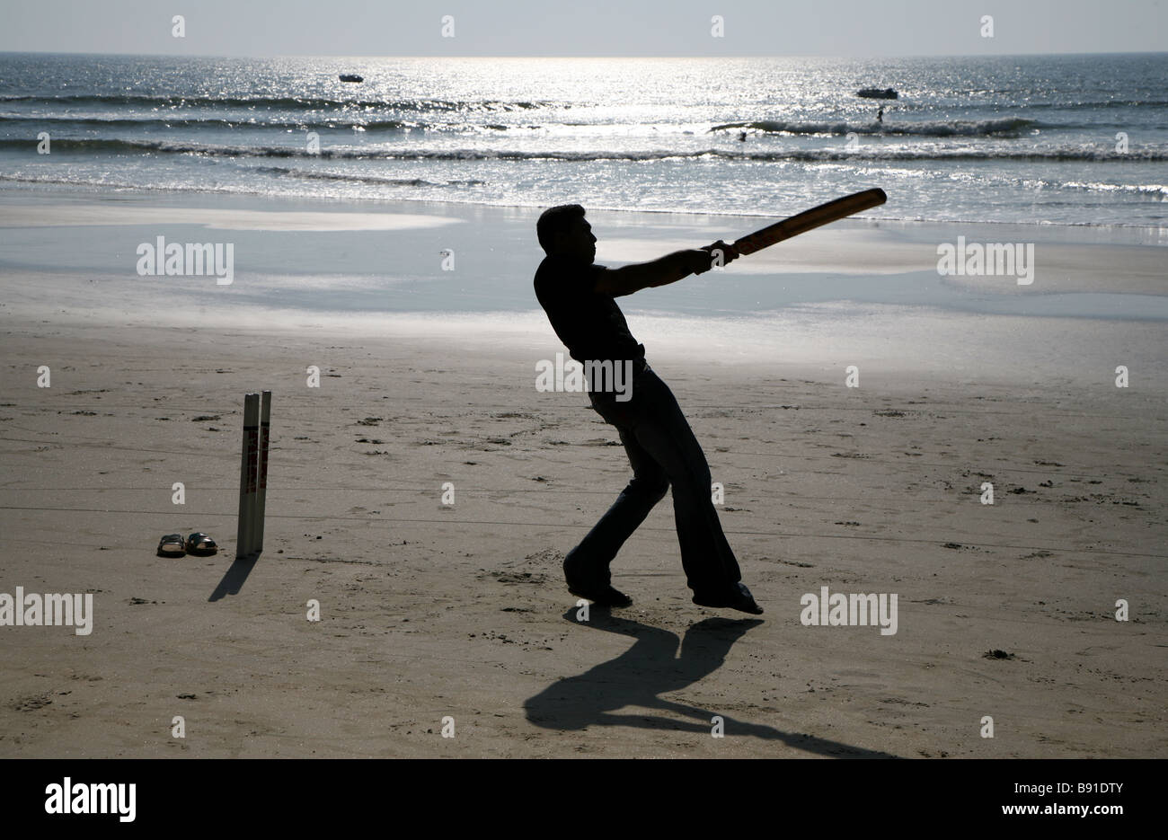 Un uomo a giocare a cricket sulla spiaggia di Mobor in Goa, India Foto Stock