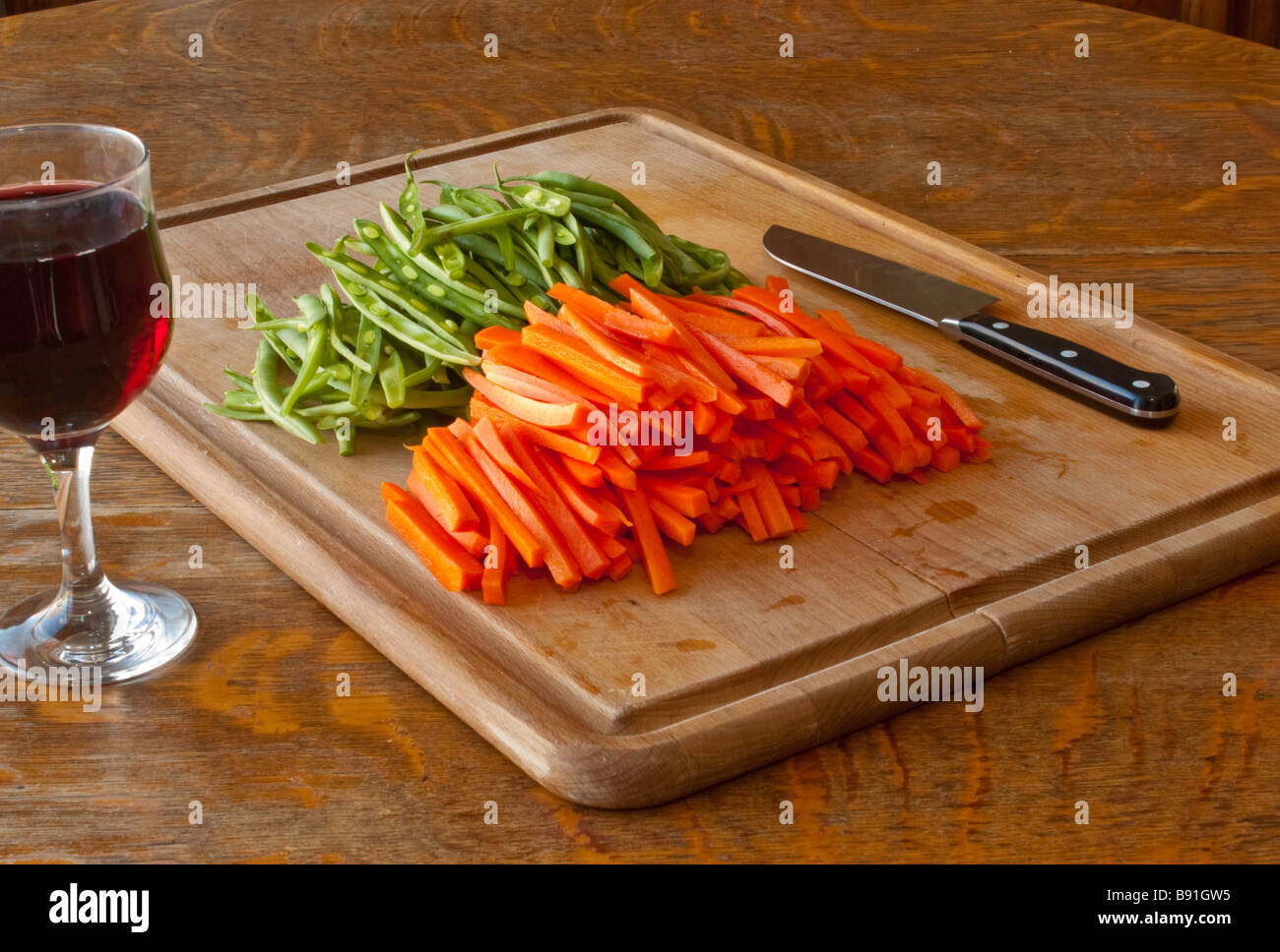 Un tagliere con tagliato in julienne le carote e i fagiolini verdi con un coltello e un bicchiere di vino per lo chef Foto Stock