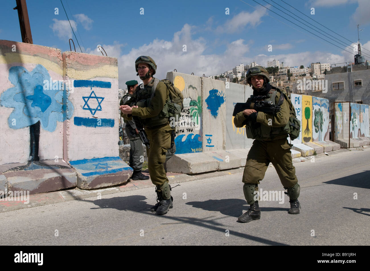 Soldati israeliani di pattuglia lungo le lastre di cemento separando quartiere palestinese di Bab a-Zawiya e H-2 controllo israeliano area in Hebron Cisgiordania Foto Stock