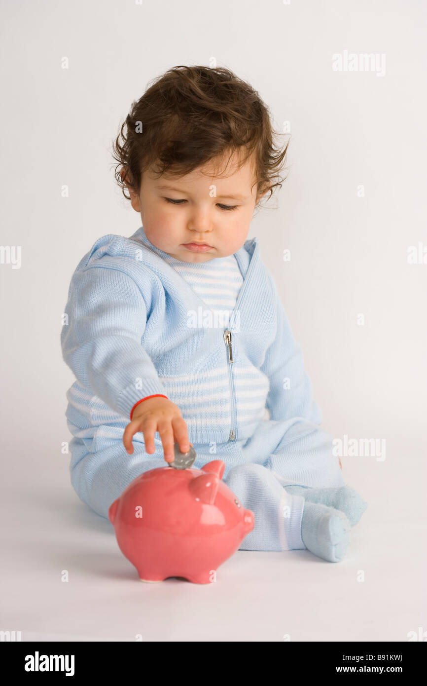 Baby boy mettendo una moneta in un salvadanaio Foto Stock