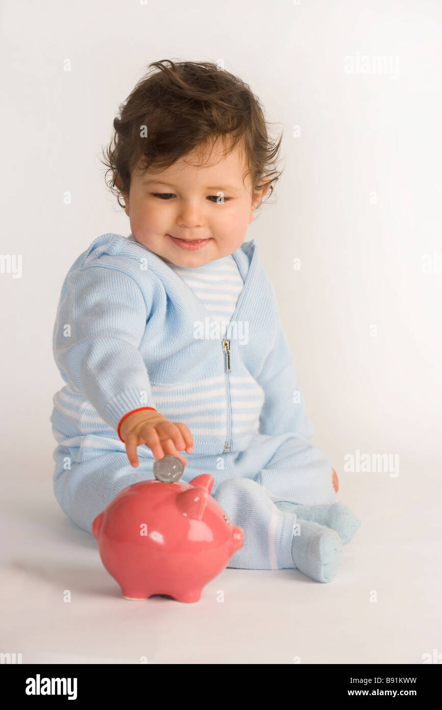 Baby boy mettendo una moneta in un salvadanaio Foto Stock