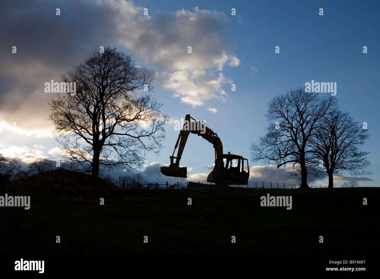 Stagliano macchina movimento terra e alberi contro il cielo nuvoloso, Cumbria, England Regno Unito Foto Stock