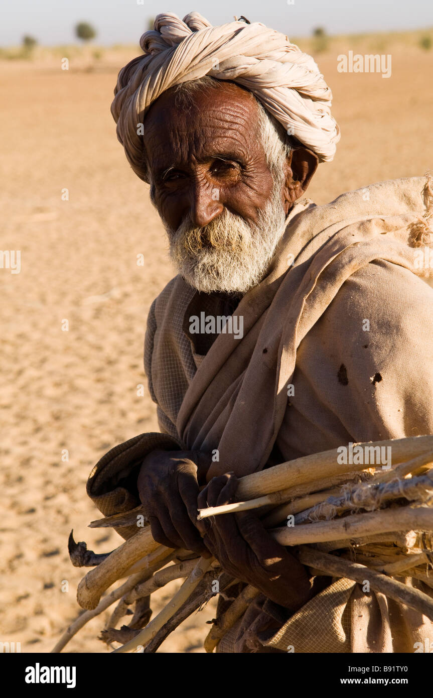 Un vecchio uomo con legno sul suo modo di tornare a casa e il legno è molto difficile da trovare da remoto in regioni di deserto di West Rajasthan, India. Foto Stock