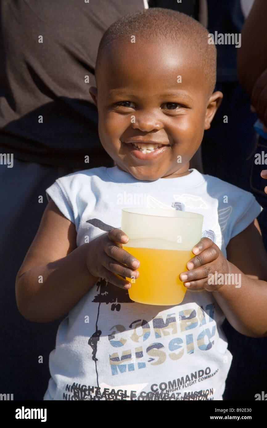 Ragazzo giovane sorride come egli si prepara a sorseggiare il suo succo di arancia Kamberg KwaZulu Natal provincia Sud Africa Foto Stock